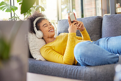 Buy stock photo Headphones, phone and happy woman on sofa, relax and home networking, social media and music streaming. Mobile app, audio electronics and young african person on couch, web listening or internet chat