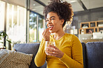 Young happy mixed race woman taking medication with water at home. One hispanic female with a curly afro taking a vitamin for good health while sitting on the couch at home. Woman drinking a supplement