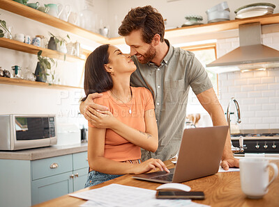Buy stock photo Young happy interracial couple bonding while going through paper and using a laptop together at home. Caucasian boyfriend and girlfriend hugging in the kitchen. Cheerful husband and wife working on a laptop together