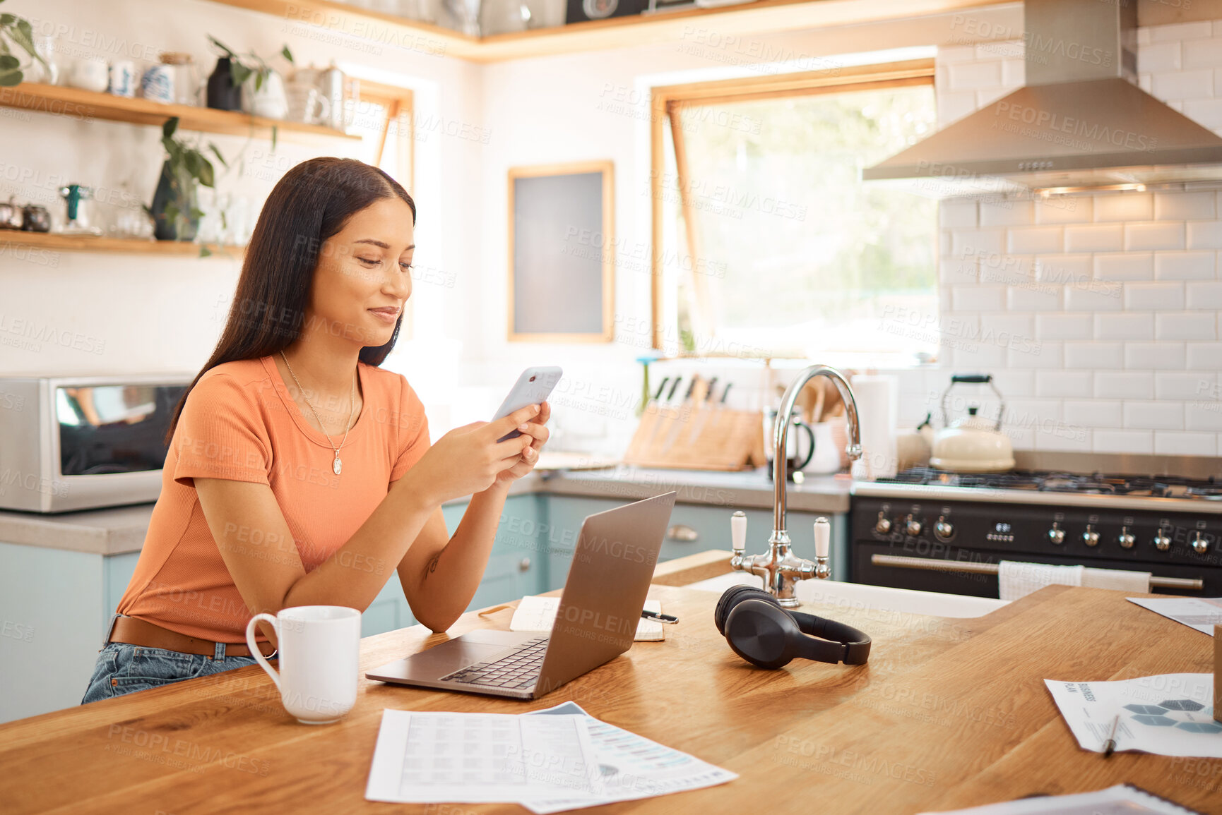 Buy stock photo Young happy mixed race businesswoman using a phone while working from home. One content hispanic woman using social media on her cellphone while using a laptop