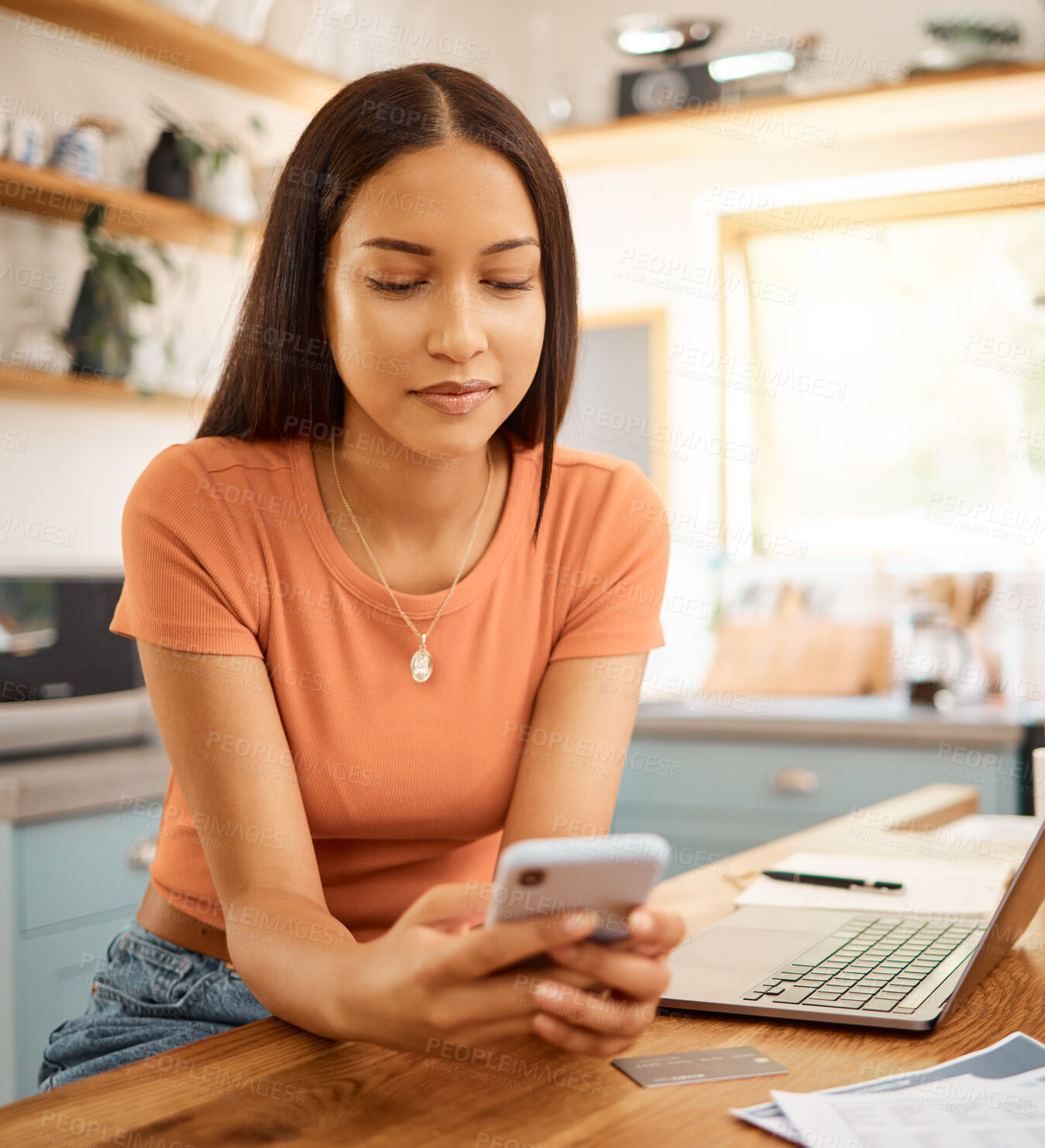 Buy stock photo Young beautiful happy mixed race businesswoman holding and using a phone while working from home. One content hispanic woman using social media on her cellphone while using a laptop