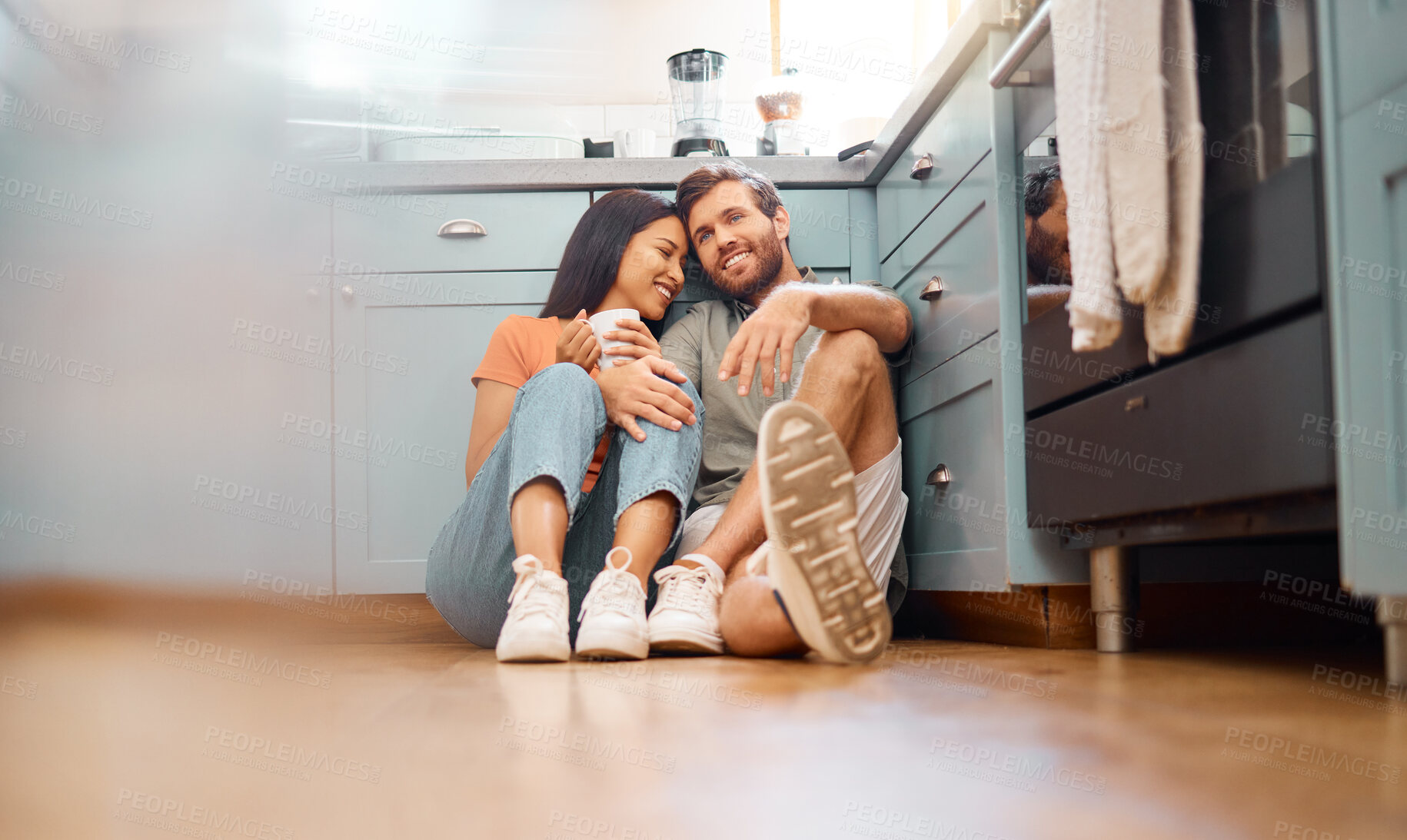 Buy stock photo Young happy interracial couple bonding while drinking coffee together at home. Loving caucasian boyfriend and mixed race girlfriend sitting on the kitchen floor. Cheerful husband and wife relaxing and spending time together