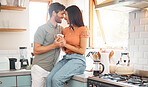 Young happy interracial couple bonding while drinking tea together at home. Loving caucasian boyfriend and mixed race girlfriend standing in the kitchen. Content husband and wife relaxing and spending time together in the morning