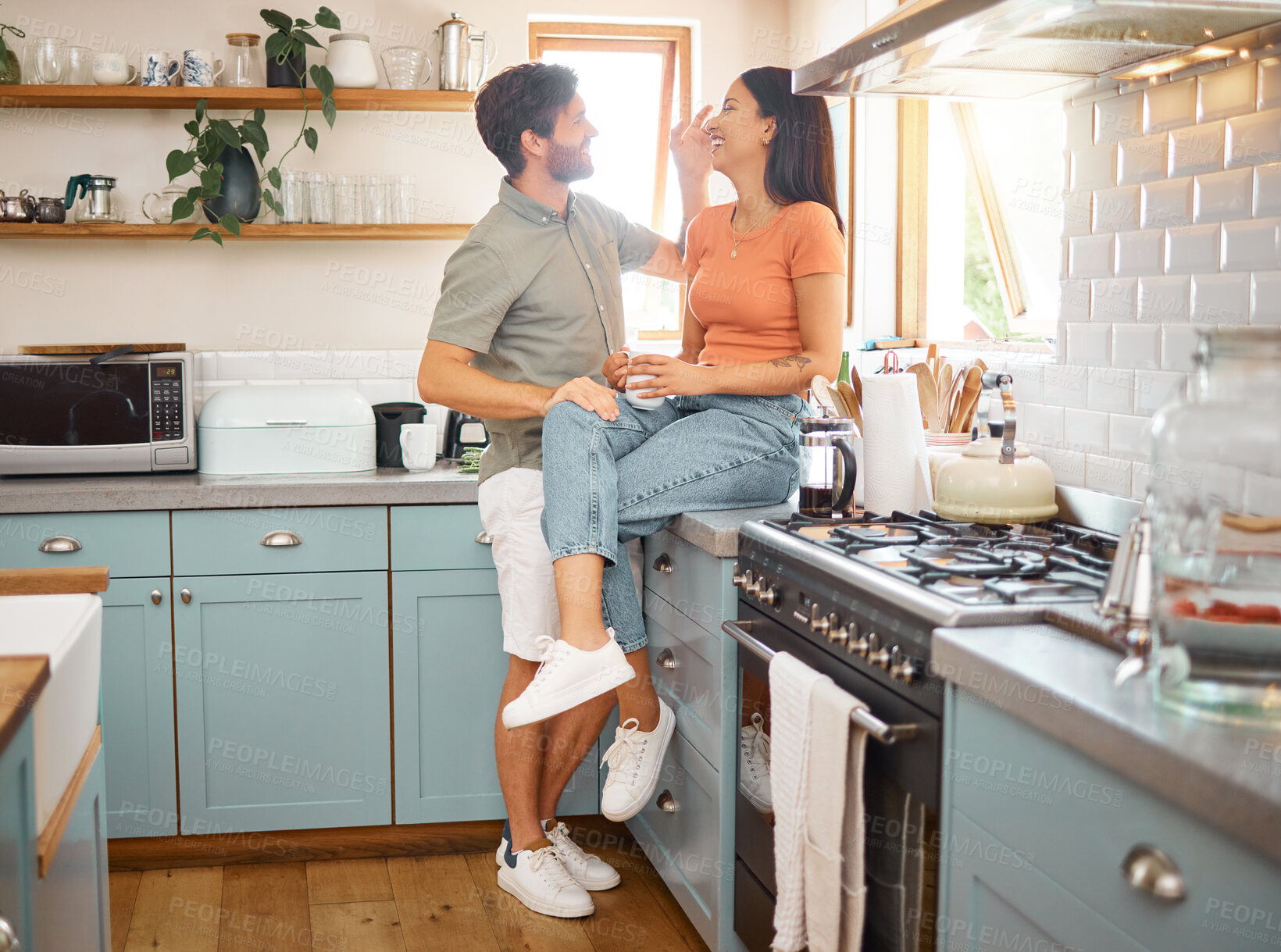 Buy stock photo Young cheerful interracial couple bonding while drinking tea together at home. Loving caucasian boyfriend and mixed race girlfriend standing in the kitchen. Content husband and wife relaxing and spending time together in the morning