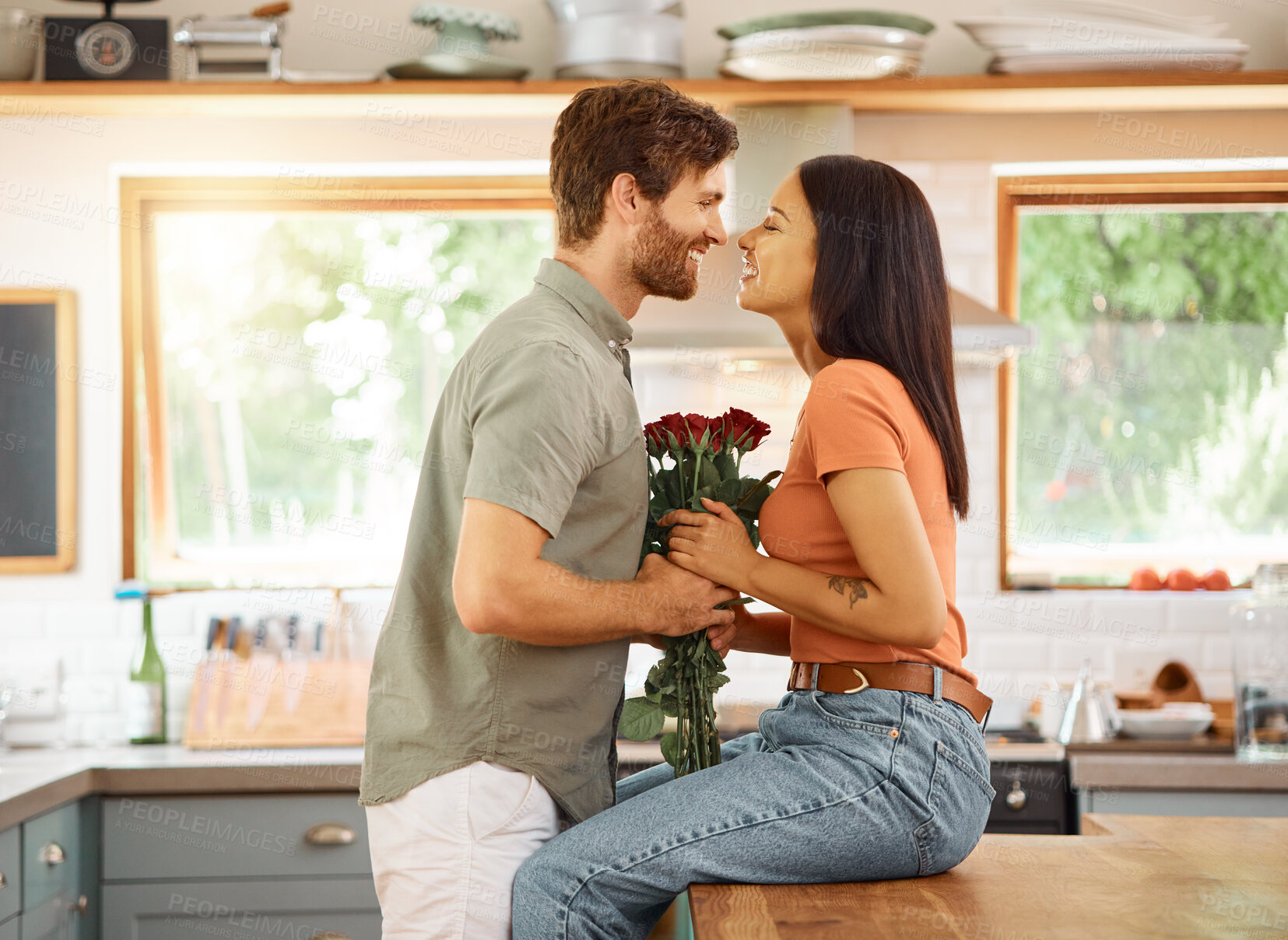Buy stock photo Young content caucasian boyfriend giving his cheerful mixed race girlfriend a bouquet of flowers at home. Happy hispanic wife receiving roses from her husband. Interracial couple bonding together at home