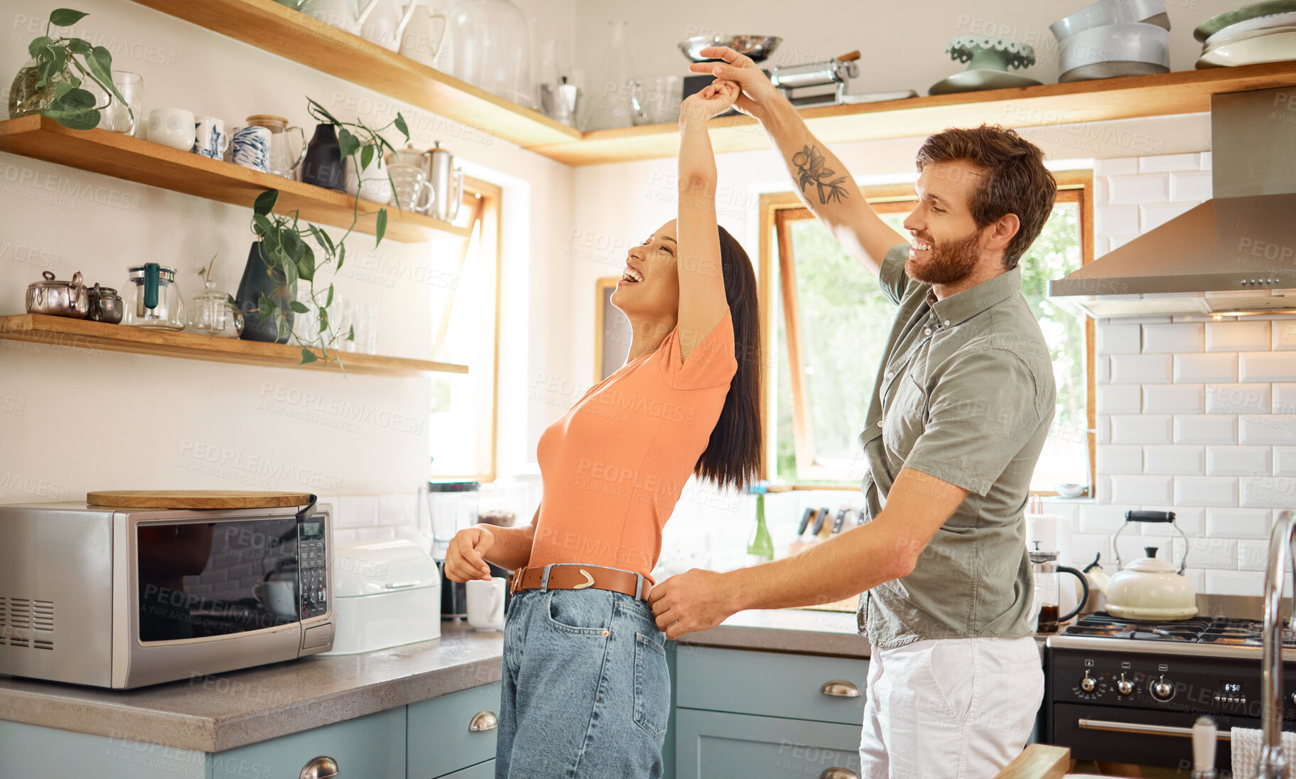 Buy stock photo Young content interracial couple dancing in the kitchen at home. Playful caucasian boyfriend and mixed race girlfriend having fun. Husband and wife relaxing and spending time together in the morning