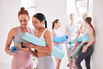 Two friends talking before yoga class. Young woman showing her friend a text on her cellphone. Friends looking at smartphone before yoga practice. Friends bonding in the yoga studio.