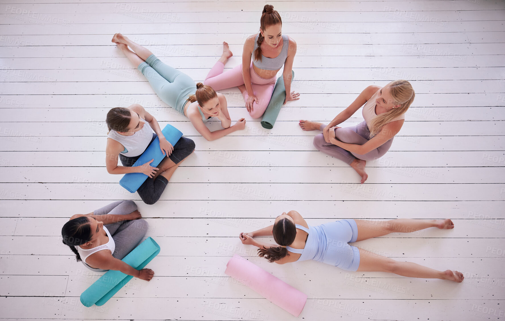 Buy stock photo Group of women relaxing in yoga class from above. Friends talking, being social in pilates class. Women bonding in yoga class. Young women sitting on the floor in yoga class from above