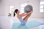 Strong woman training her core with a ball. Young woman using exercise ball in yoga studio. Dedicated using exercise ball to balance. Fit woman exercise her abs in pilates class