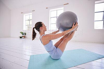 Strong woman training her core with a ball. Young woman using exercise ball in yoga studio. Dedicated using exercise ball to balance. Fit woman exercise her abs in pilates class