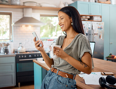 One happy young mixed race woman standing in her kitchen at home and using a cellphone to browse the internet while drinking a cup of coffee. Smiling hispanic reading message on social media and networking on a phone