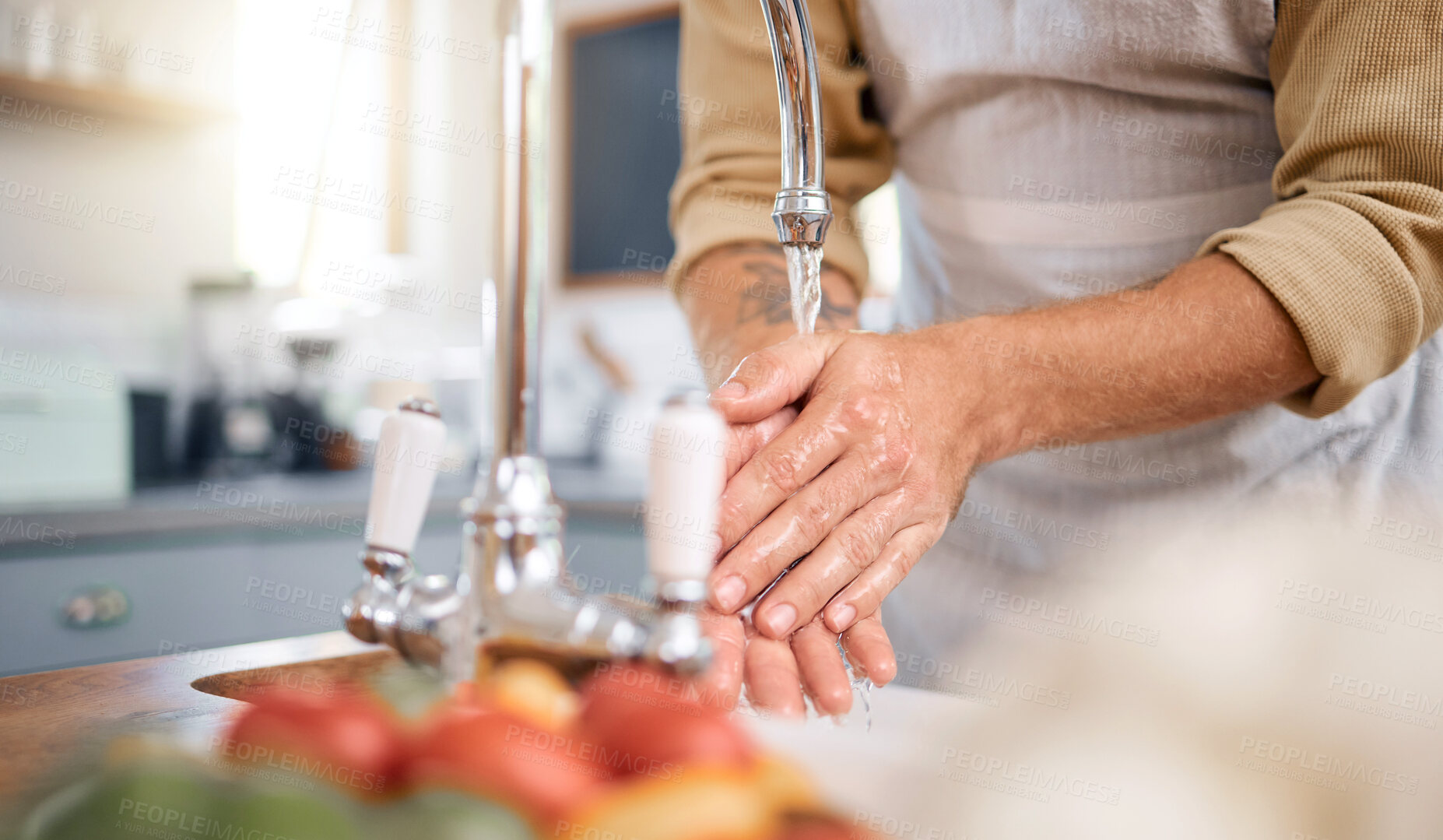 Buy stock photo Close up of a man wearing an apron and washing his hands in sink with tap water in the kitchen at home. Always wash your hands before cooking