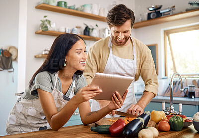 Happy young interracial couple using digital tablet while cooking together at home. Young caucasian man cutting vegetables while hispanic wife reads recipe on web