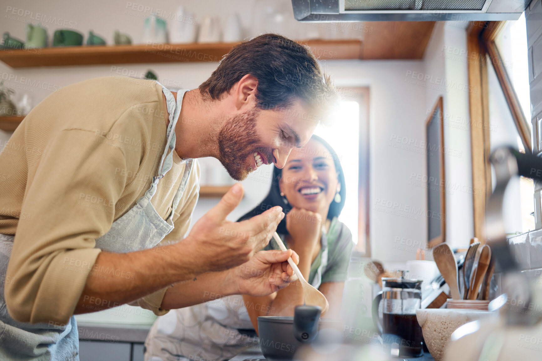 Buy stock photo Happy young interracial couple standing by the stove while cooking together in the kitchen at home. Young caucasian man looking and smelling steamy food while it cooks on the stove