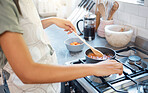 Close up of female hands preparing food on the stove in the kitchen at home. Unrecognizable woman holding spoon and stirring sauce while cooking