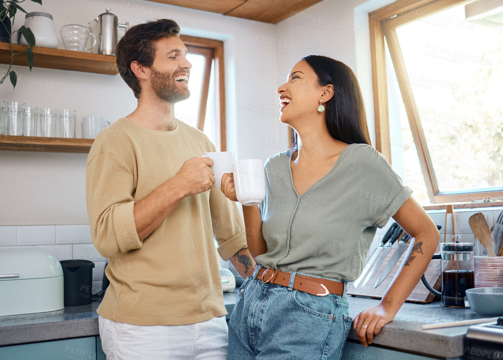 Buy stock photo Loving young interracial couple drinking their morning coffee and talking while standing in the kitchen at home. Young man and woman looking happy to be together in healthy relationship