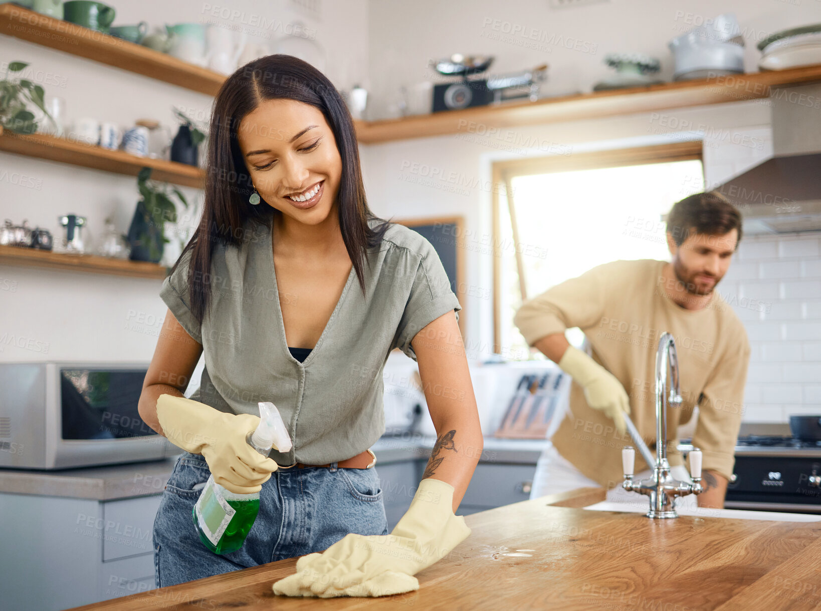 Buy stock photo Happy young interracial couple cleaning their home. Young man and woman wearing gloves while doing chores together at home. Hispanic female cleaning kitchen counter while her husband mops in the background