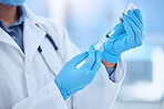 doctor wearing gloves and preparing a vaccine by removing liquid out of a vial with a syringe while working at a hospital. A doctor removing fluid from a vial with a syringe at a clinic