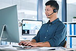 One happy hispanic call centre telemarketing agent talking on a headset while working on a computer in an office. Confident friendly male consultant operating a helpdesk for customer service and sales support