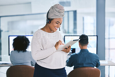 Buy stock photo Young african american businesswoman browsing on a digital tablet device while working in a call centre with her colleagues in the background. Happy manager and supervisor planning online with smart apps for customer service support