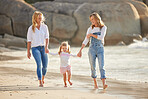 Cute caucasian girl being held outside by her mom and grandmother in the sea at the beach. A young woman and her mom holding cute daughter while walking in the water on the coast at sunset