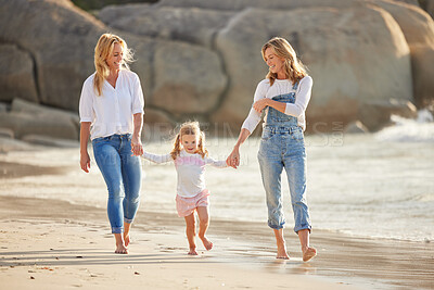 Buy stock photo Cute caucasian girl being held outside by her mom and grandmother in the sea at the beach. A young woman and her mom holding cute daughter while walking in the water on the coast at sunset