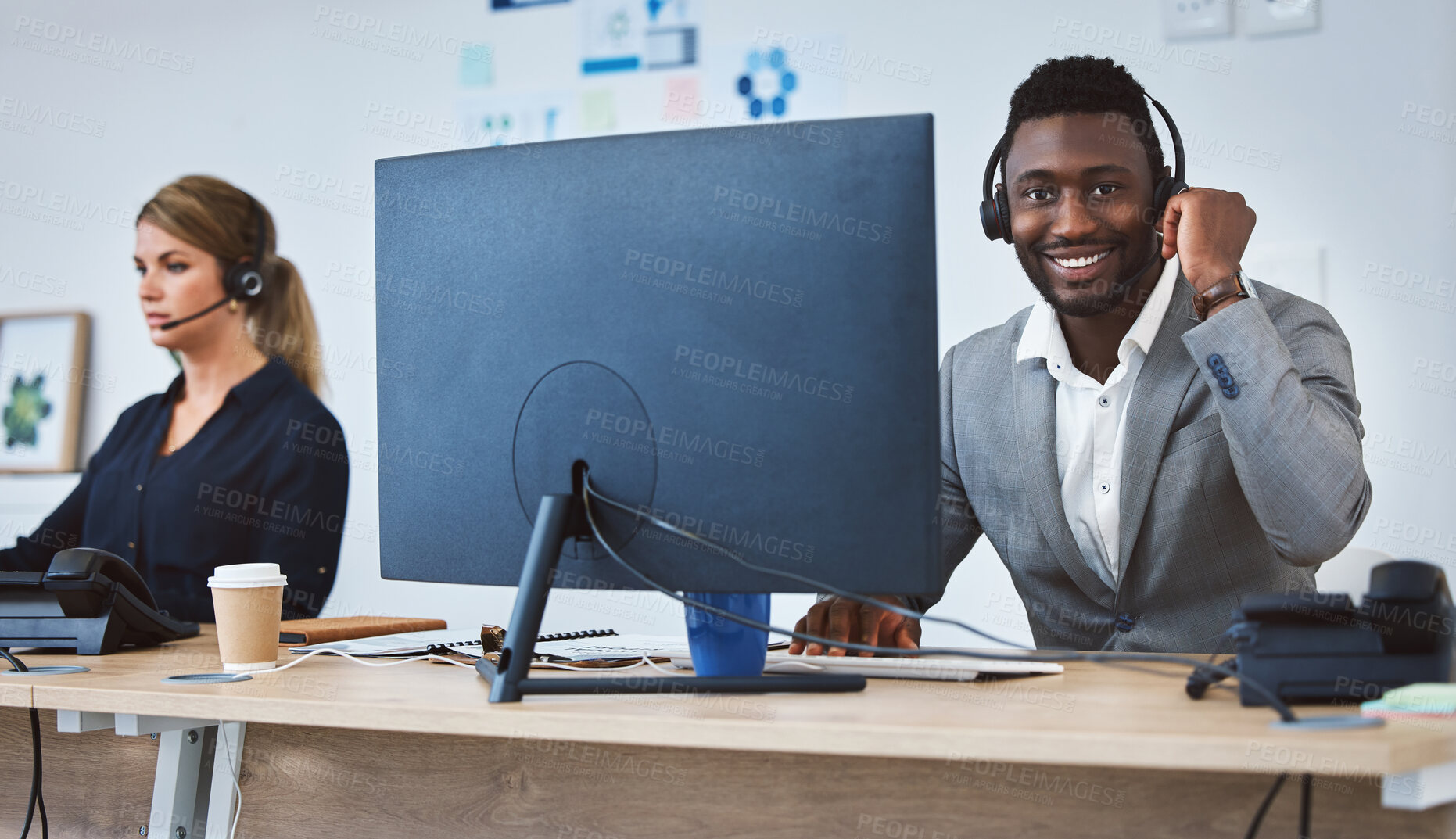 Buy stock photo Portrait of happy young african american call centre telemarketing agent talking on a headset while working on computer alongside a colleague in an office. Confident friendly male consultant operating helpdesk for customer service and sales support