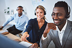 Happy african american male call centre telemarketing agent discussing plans with diverse colleagues while working together on computer in an office. Consultants troubleshooting solution for customer service and sales support