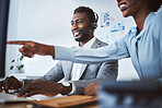 Happy african american male call centre telemarketing agent discussing plans with colleague while working together on computer in an office. Two consultants troubleshooting solution for customer service and sales support