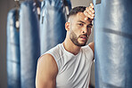 Portrait of tired boxer leaning on punching bag. Exhausted mma fighter resting after workout in the gym. Bodybuilder boxing routine in the gym. Strong fit man tired after combat training