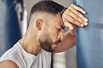 Exhausted boxer resting after workout routine. Tired mma fighter taking a break from exercise routine. Combat fighter leaning on punching bag. Strong athlete relaxing after workout