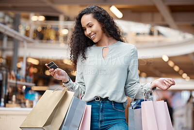 One beautiful mixed race woman holding a credit card and standing in a mall shopping. Young hispanic woman carrying bags, spending money, looking for sales and getting in some good retail therapy
