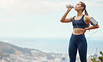 One fit young mixed race woman taking a rest break to drink water from bottle while exercising outdoors. Female athlete wearing earphones and armband quenching thirst and cooling down after running and training workout