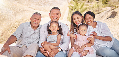 Portrait of a smiling mixed race family with little girls sitting together at the beach. Adorable little kids bonding with their parents and grandparents while having a picnic at a park or garden