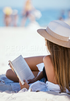 One beautiful young caucasian woman relaxing on the beach. Enjoying a summer vacation or holiday outdoors during summer. Taking time off and getting away from it all. Reading alone on the sand outside