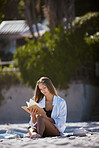 One beautiful young caucasian woman relaxing on the beach. Enjoying a summer vacation or holiday outdoors during summer. Taking time off and getting away from it all. Reading alone on the sand outside