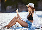 One beautiful young caucasian woman relaxing on the beach. Enjoying a summer vacation or holiday outdoors during summer. Taking time off and getting away from it all. Reading alone on the sand outside