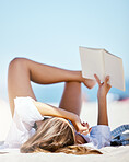 One beautiful young caucasian woman relaxing on the beach. Enjoying a summer vacation or holiday outdoors during summer. Taking time off and getting away from it all. Reading alone on the sand outside