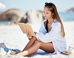 One beautiful young caucasian woman relaxing on the beach. Enjoying a summer vacation or holiday outdoors during summer. Taking time off and getting away from it all. Reading alone on the sand outside