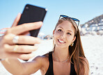 One beautiful young caucasian woman relaxing and taking a selfie on her phone while sitting on the beach. Enjoying a summer vacation or holiday outdoors. Taking time off and getting away from it all