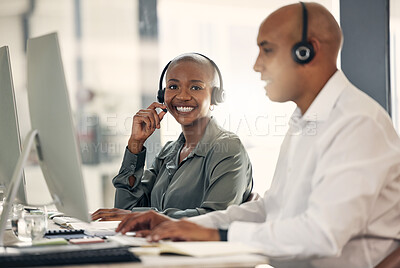 Buy stock photo Portrait of happy young african american call centre telemarketing agent talking on a headset while working on a computer in an office alongside a colleague. Confident friendly female consultant operating helpdesk for customer service and sales support