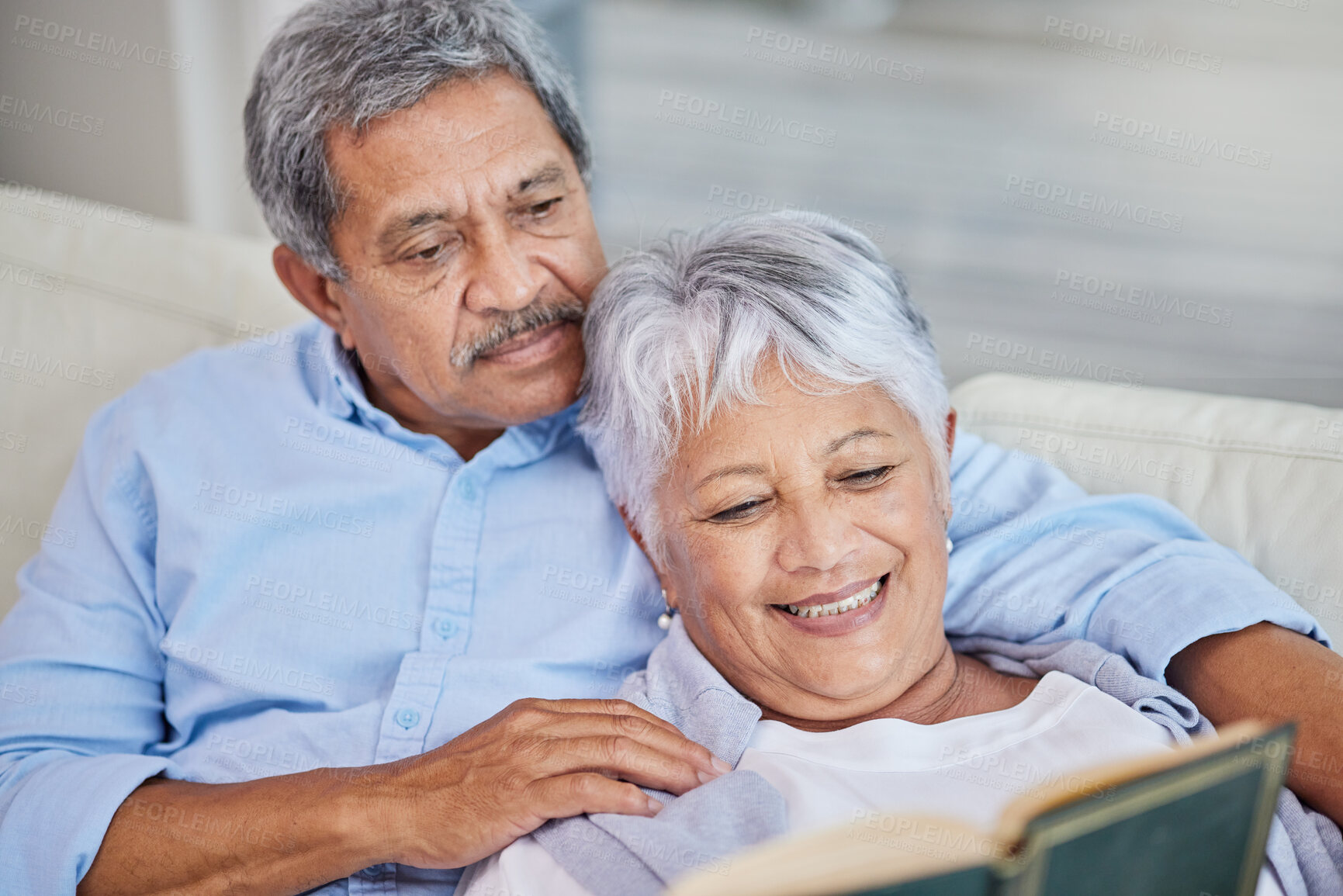 Buy stock photo Closeup of an affectionate mixed race senior couple relaxing and reading a book in their living room at home. Hispanic man and wife  bonding on the sofa in the living room being affectionate