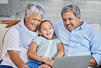 Closeup of an affectionate mixed race senior couple relaxing in their living room with their granddaughter using a laptop. Hispanic man and wife  bonding on the sofa in the living room being affectionate and using a wireless device