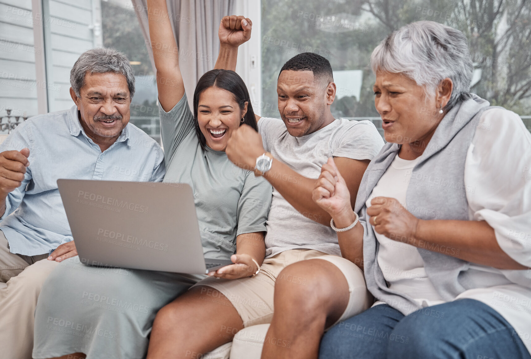 Buy stock photo Happy and affectionate mixed race family of four using a laptop to watch sports and cheer on their favourite team in the home living room. Married couple sitting with their mature parents on the sofa