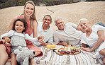 Portrait of a mixed race family having a picnic on the beach and smiling while having some food with snacks. Happy family bonding on a day out at the beach