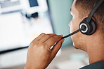 Closeup of one mixed race call centre telemarketing agent from behind talking on a headset while working on a computer in an office. Hands and face of male consultant operating a helpdesk for customer service and sales support