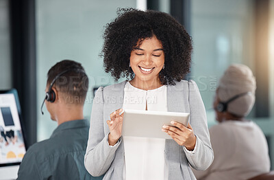 Young mixed race businesswoman browsing on a digital tablet device while working in a call centre with her colleagues in the background. Happy manager and supervisor planning online with smart apps for customer service support