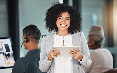 Portrait of young mixed race businesswoman browsing on a digital tablet device while working in a call centre with her colleagues in the background. Happy manager and supervisor planning online with smart apps for customer service support