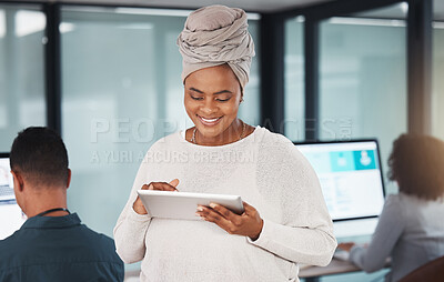 Confident young african american businesswoman browsing on a digital tablet device while working in an office with her colleagues in the background. Happy manager and supervisor planning online with smart apps