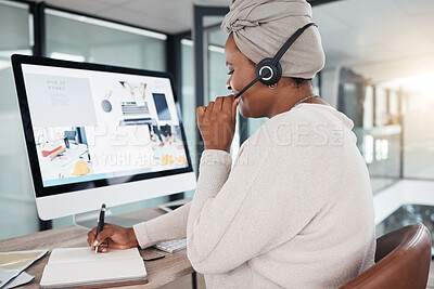 One african american call centre telemarketing agent from the back talking on a headset while writing notes and working on a computer in an office. Female consultant operating a helpdesk for customer service and sales support